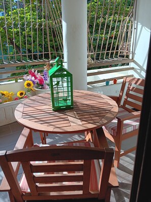 Ein runder Holztisch mit Stühlen, eine grüne Laterne und Topfpflanzen auf einem Balkon.