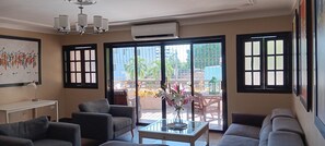 Sala de estar com sofá, mesa de centro e quadro na parede. Ampla janela com vista para o exterior.