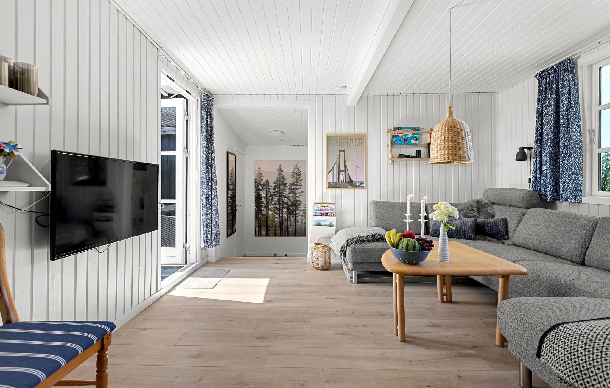 Una sala de estar moderna con una televisión de pantalla plana, un sofá gris, una mesa de centro de madera y una lámpara colgante de mimbre.