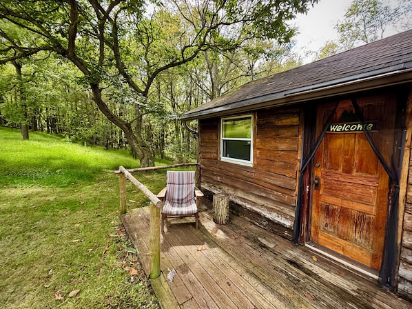 A wooden cabin with a porch, a striped chair, and a 'Welcome' sign.