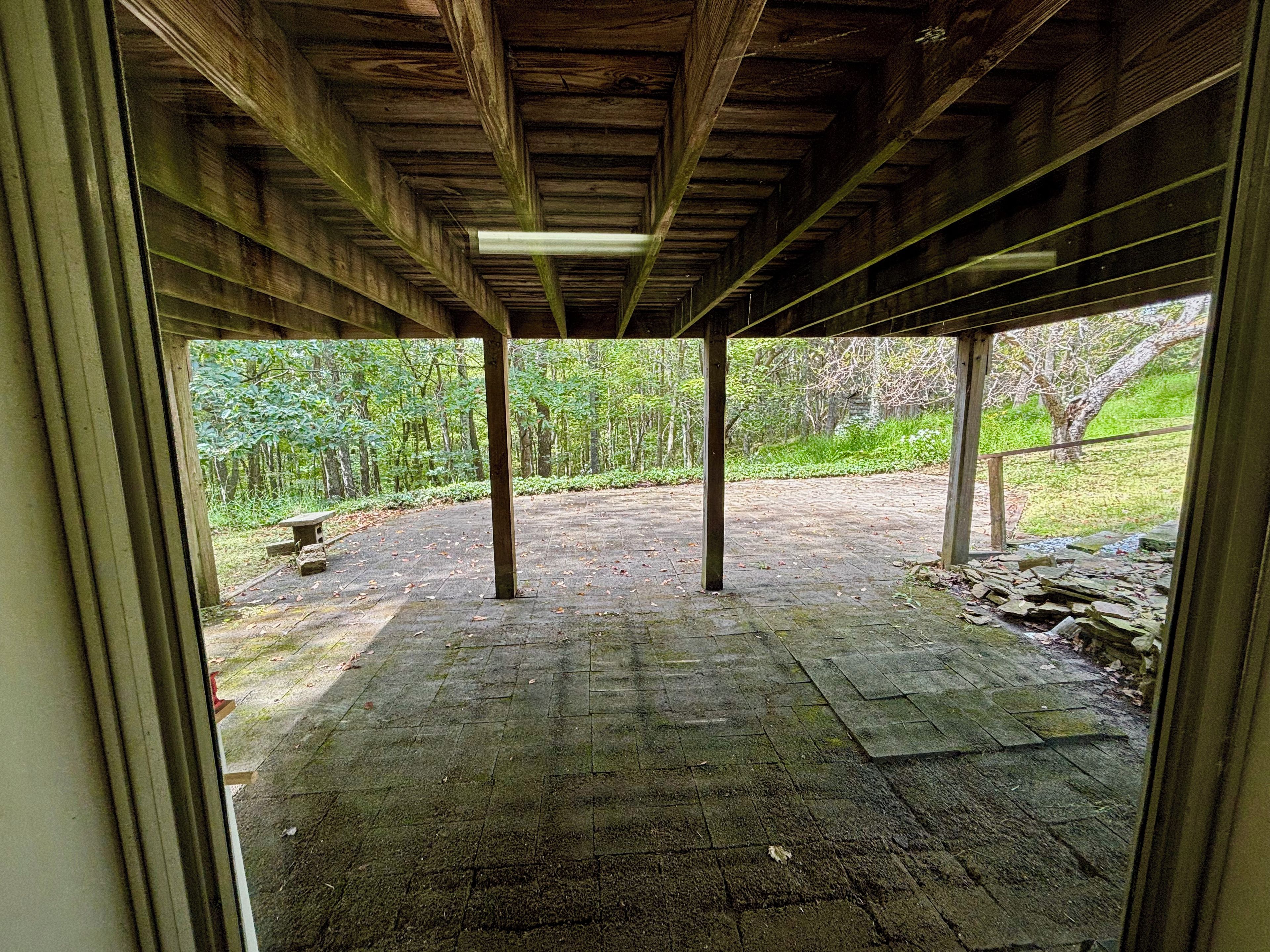 An open wooden structure with a view of a paved area and greenery outside.