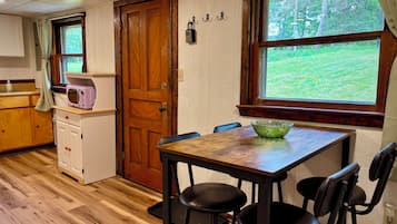 A kitchen with wooden cabinets, a microwave, a wooden door, and a window with a view of greenery.