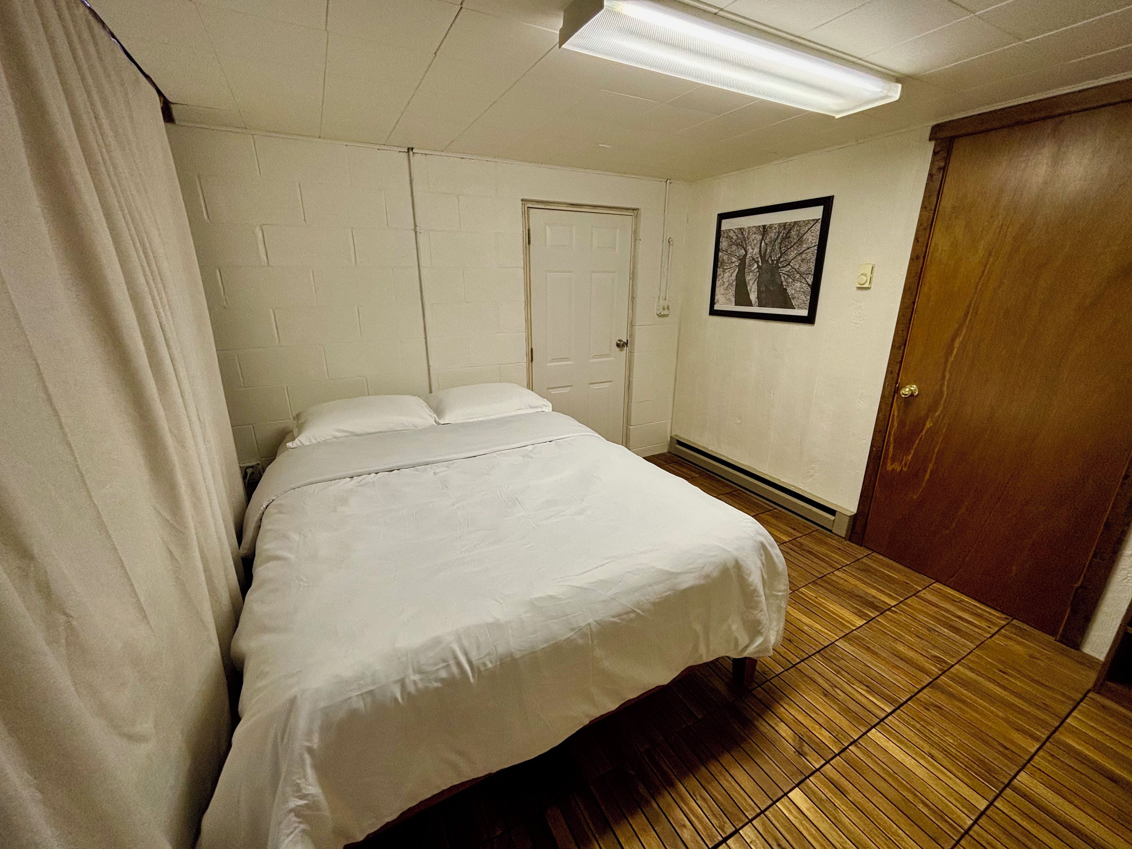 A hotel room with a bed, a door, a framed picture on the wall, and a wooden floor.