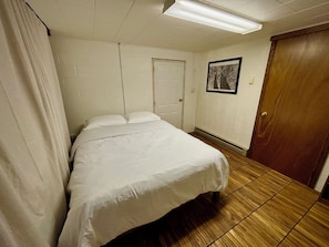 A hotel room with a bed, a door, a framed picture on the wall, and a wooden floor.