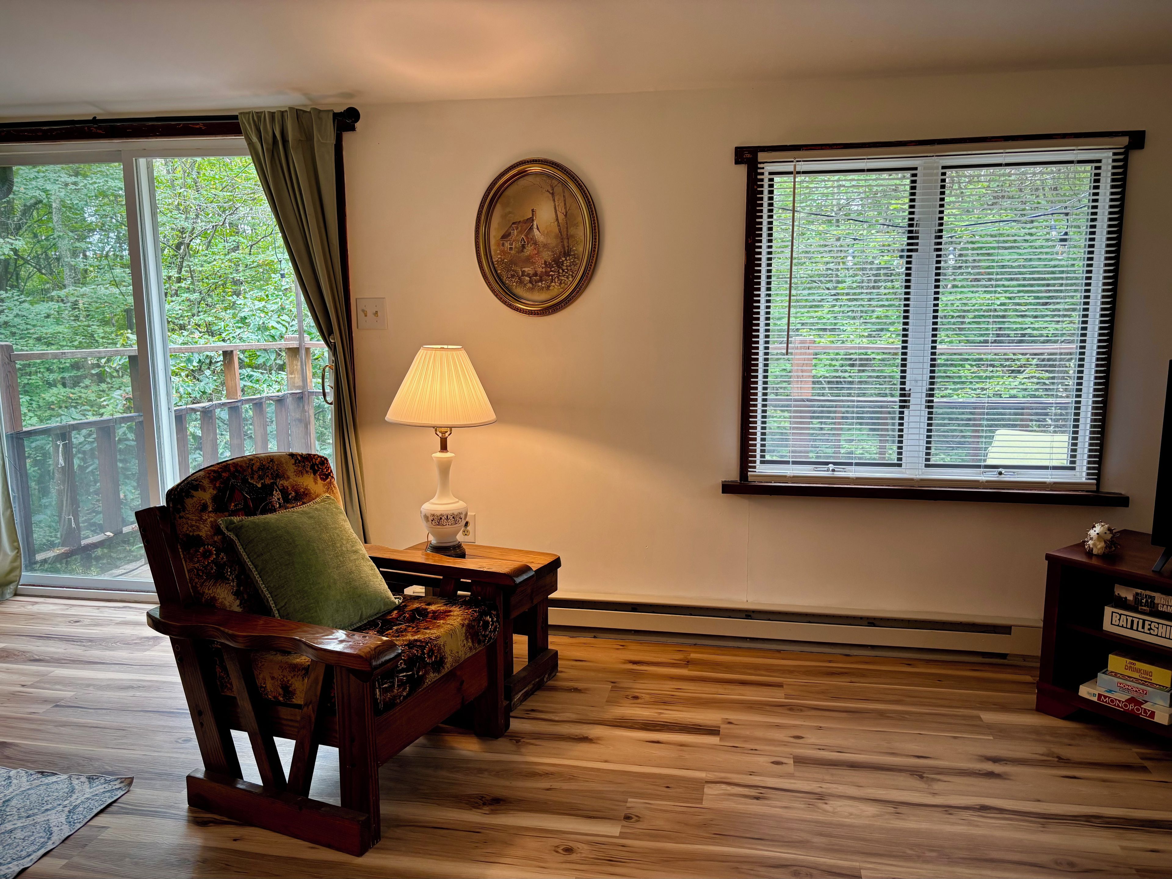 Une pièce avec un banc en bois, une table avec une lampe, un tableau au mur et une fenêtre avec des stores.