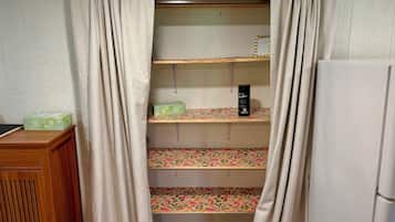 A room with a wooden cabinet, a white refrigerator, and a shelf unit with patterned fabric.