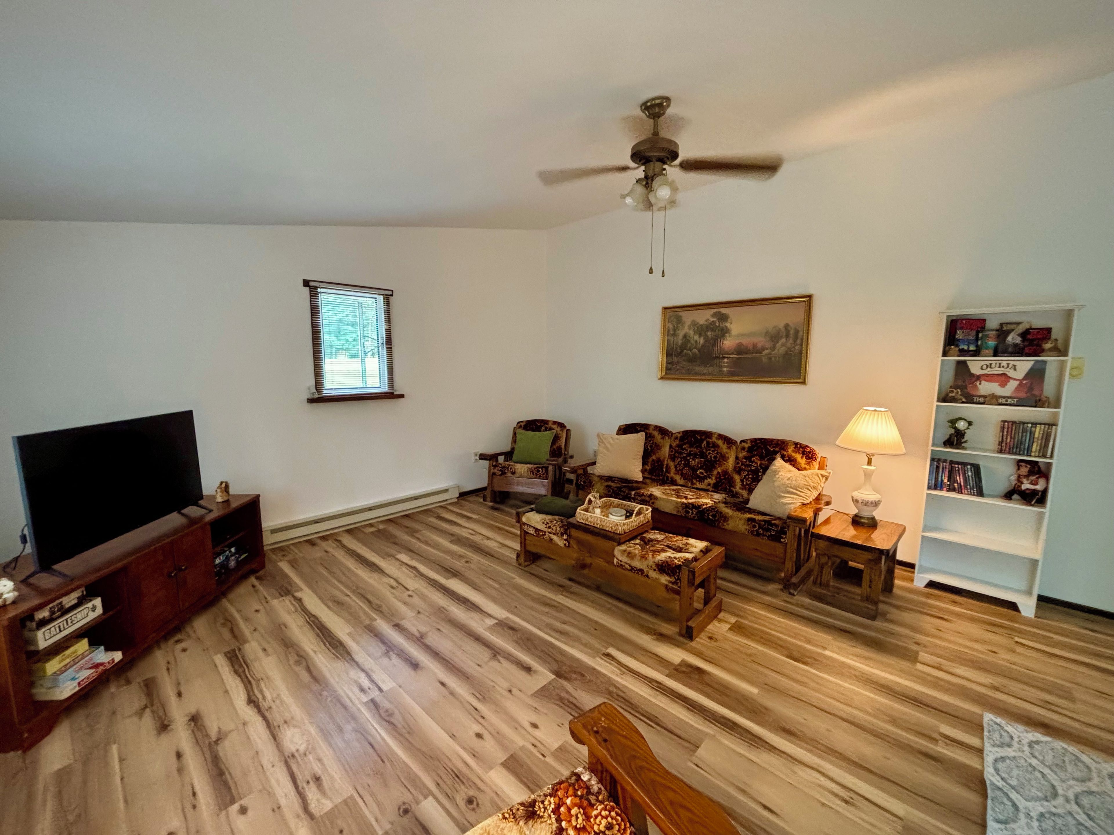 A living room with a flat-screen TV, a ceiling fan, a sofa, a coffee table, and a bookshelf.