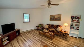 A living room with a flat-screen TV, a ceiling fan, a sofa, a coffee table, and a bookshelf.