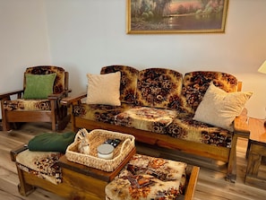 A cozy living room with a floral sofa, two armchairs, a small table with a basket, and a painting on the wall.