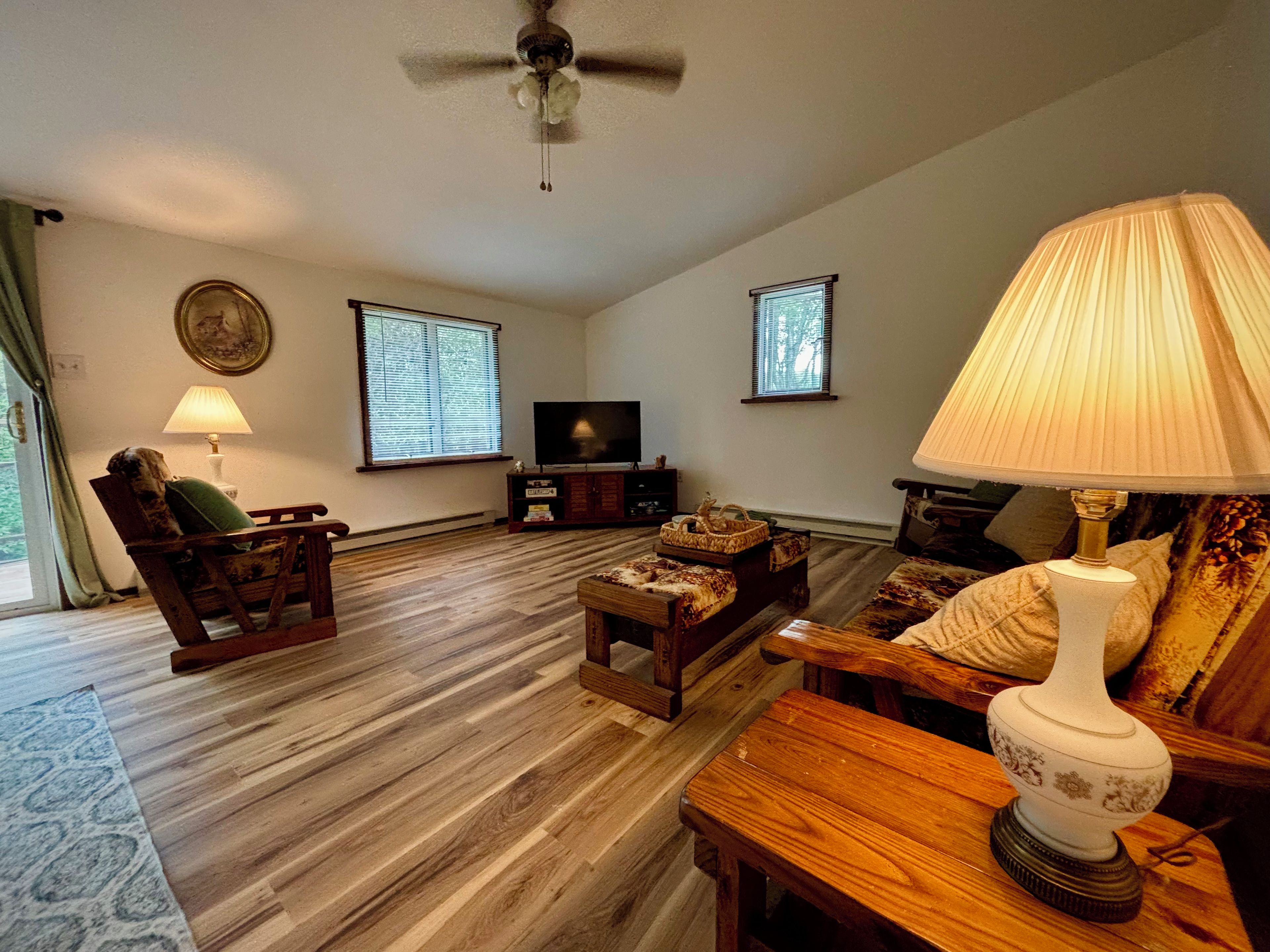 A living room with a wooden floor, a ceiling fan, a television, and a lamp.