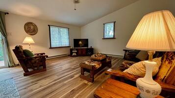 A living room with a wooden floor, a ceiling fan, a television, and a lamp.