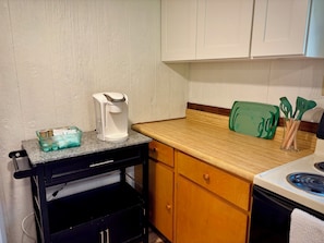 A kitchen with a coffee maker, a green cutting board, and kitchen utensils on the counter.
