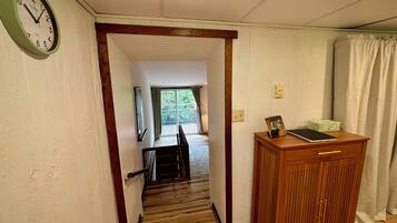 A hallway with a wooden floor, a wooden desk with a picture frame, a clock, and a window with curtains.