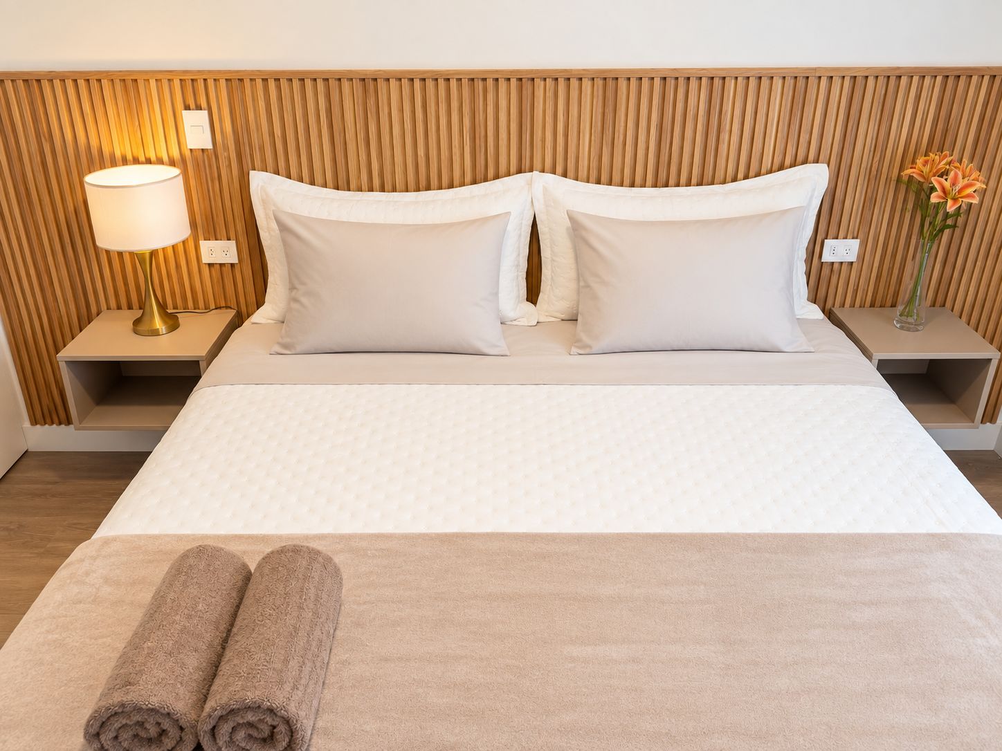 A hotel room with a bed, two bedside tables, a lamp, and a vase with flowers.