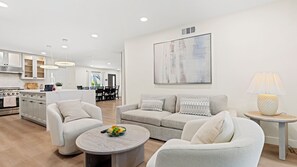 Ein modernes Wohnzimmer mit einer Couch, Sesseln, einem Couchtisch und einem Essbereich im Hintergrund.