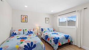 Una habitación con dos camas, una ventana con cortinas, una lámpara de pared y un cuadro enmarcado.
