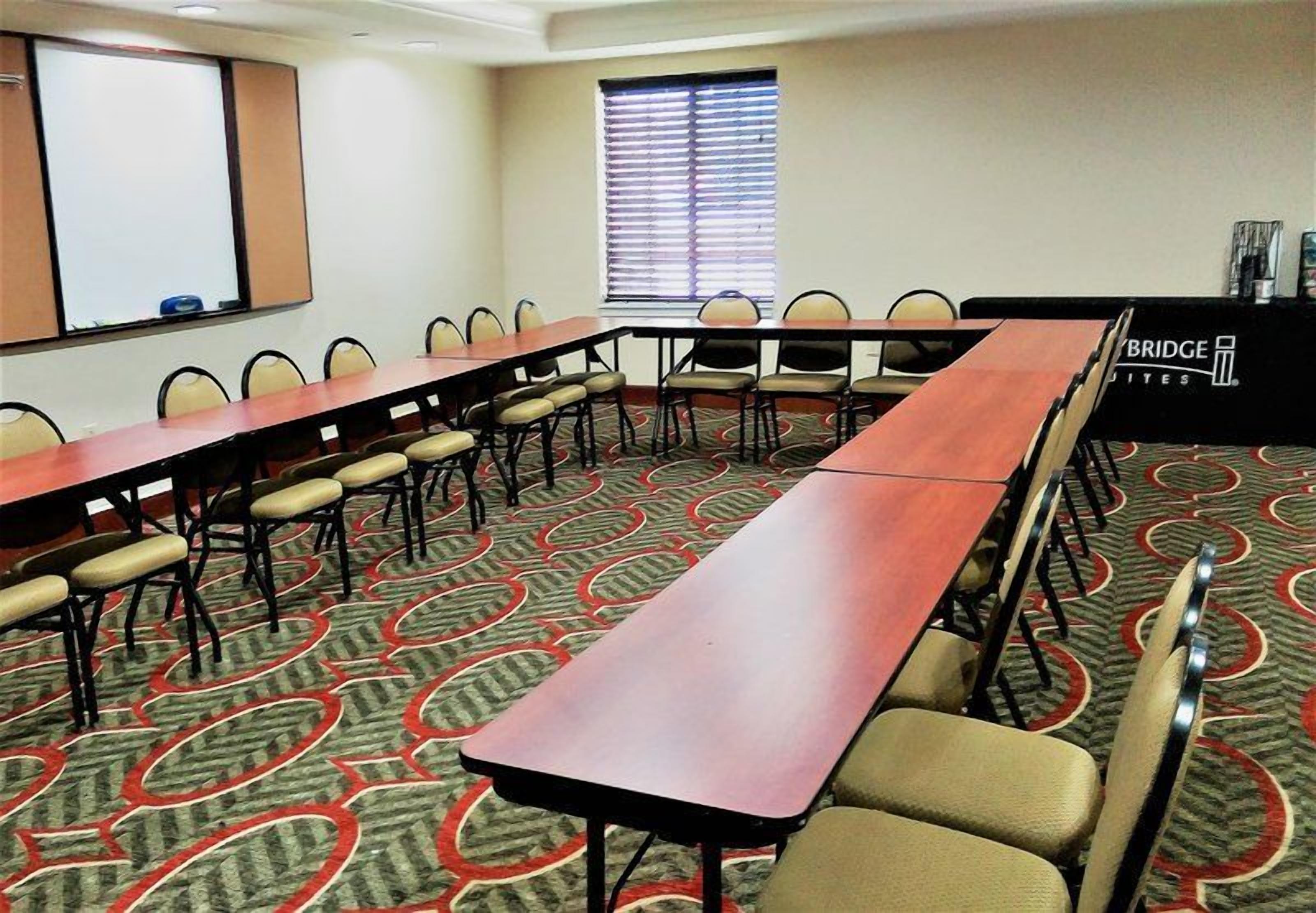 Uma sala de conferências com uma mesa comprida, cadeiras, um projetor e uma janela com persianas.