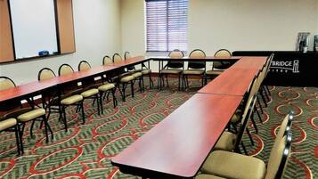 Uma sala de conferências com uma mesa comprida, cadeiras, um projetor e uma janela com persianas.
