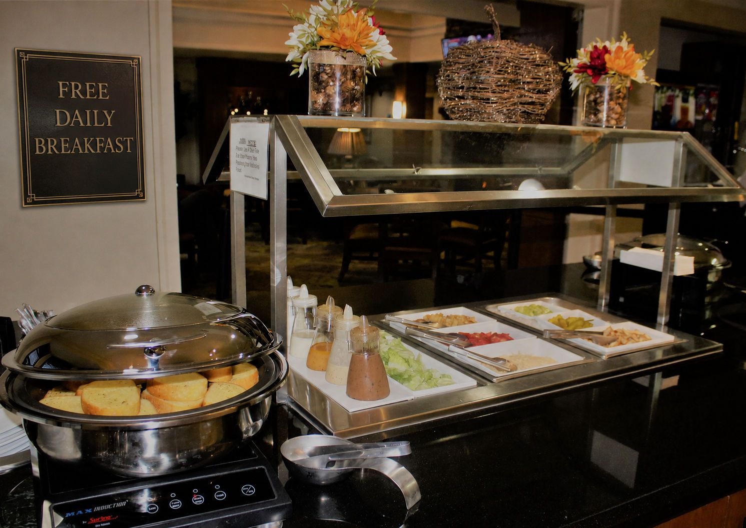 Ein reichhaltiges Buffet mit Schild für das kostenlose tägliche Frühstück, verschiedenen Speisen, Beilagen und dekorativen Blumen.
