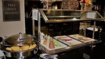 Ein reichhaltiges Buffet mit Schild für das kostenlose tägliche Frühstück, verschiedenen Speisen, Beilagen und dekorativen Blumen.