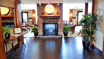 A lobby with a stone fireplace, potted plants, and a sign that reads 'BE OUR GUEST.'