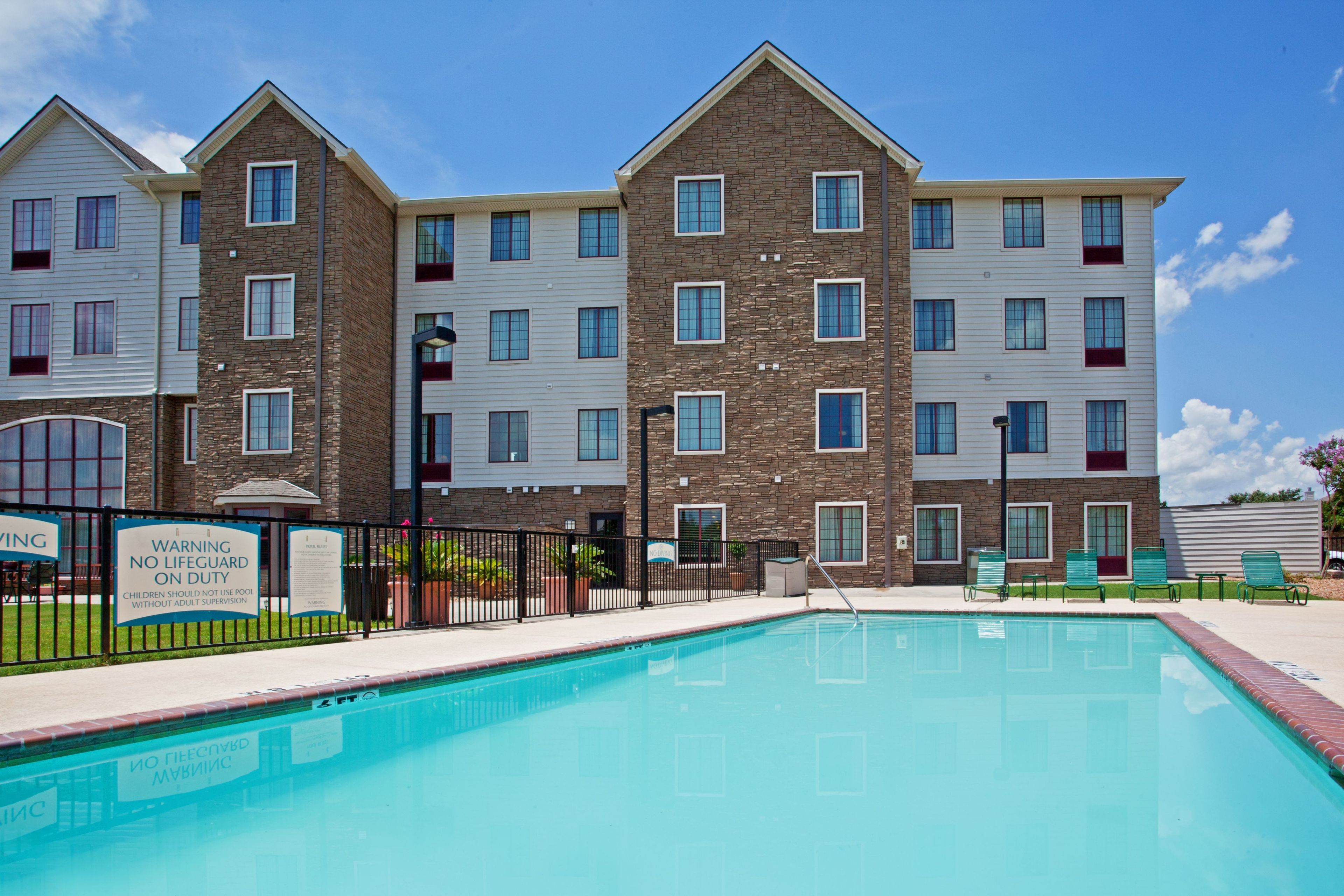 A multi-story hotel with a swimming pool, a fenced area, and a warning sign.