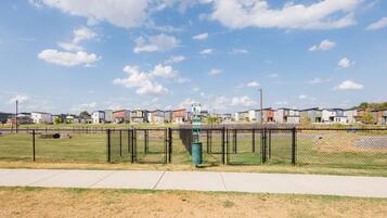 A fenced sports field with a playground and a trash can.