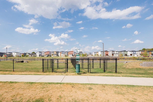 A fenced sports field with a playground and a trash can.