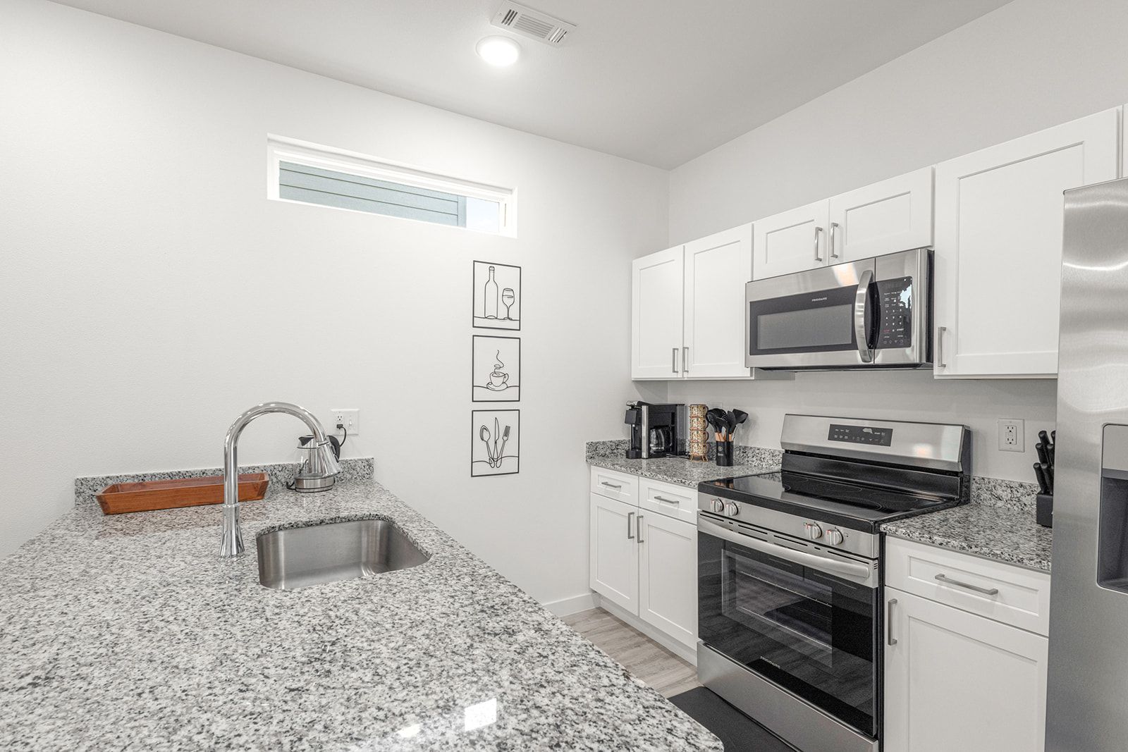 A modern kitchen with white cabinets, stainless steel appliances, granite countertops, and a built-in oven.