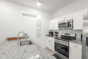 A modern kitchen with white cabinets, stainless steel appliances, granite countertops, and a built-in oven.