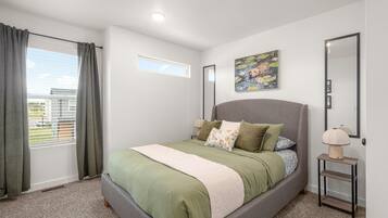 A bedroom with a bed, curtains, a window, a painting, and a nightstand.
