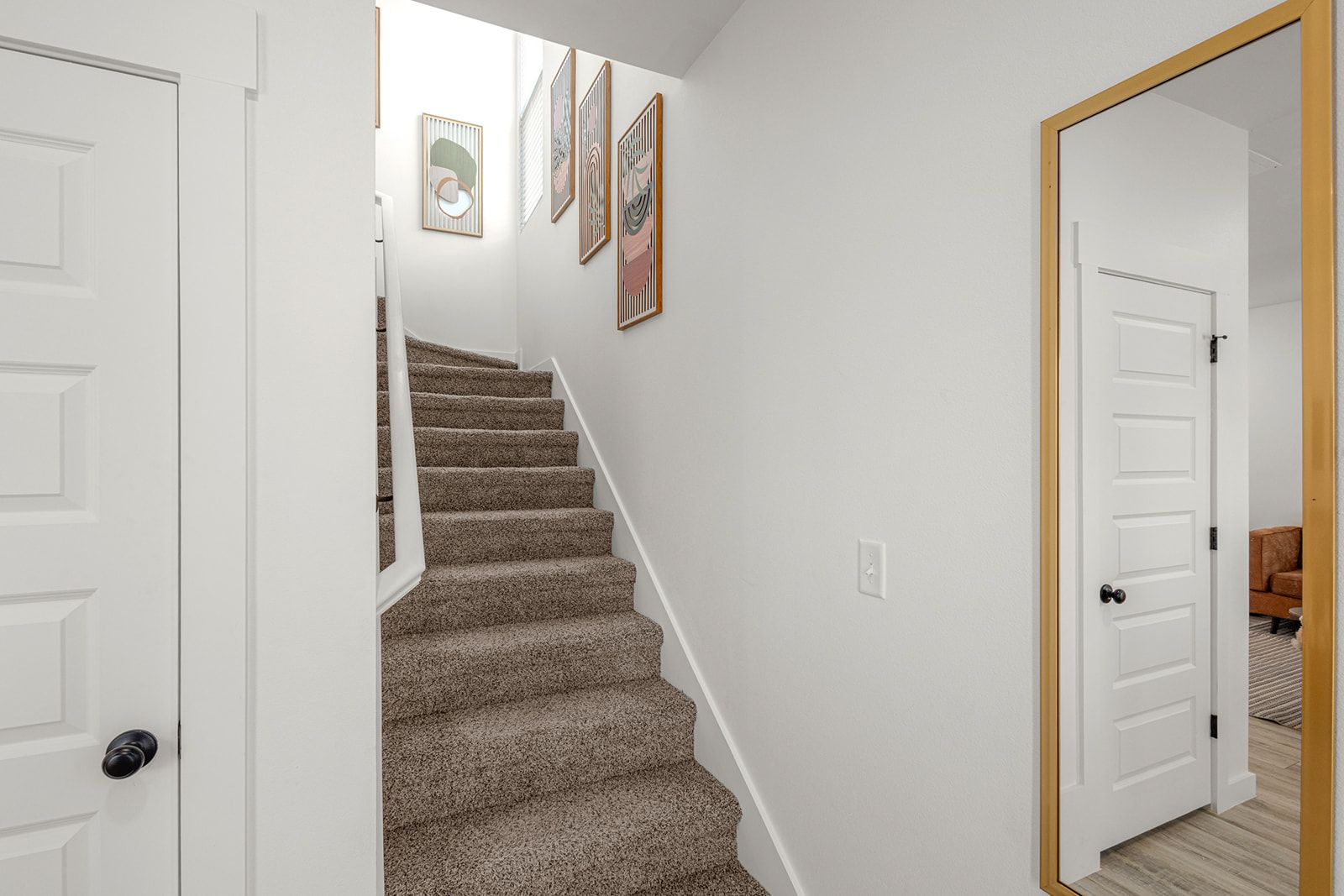 A staircase with carpeted steps leading to a landing, white walls, and a door leading to another room.