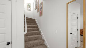 A staircase with carpeted steps leading to a landing, white walls, and a door leading to another room.
