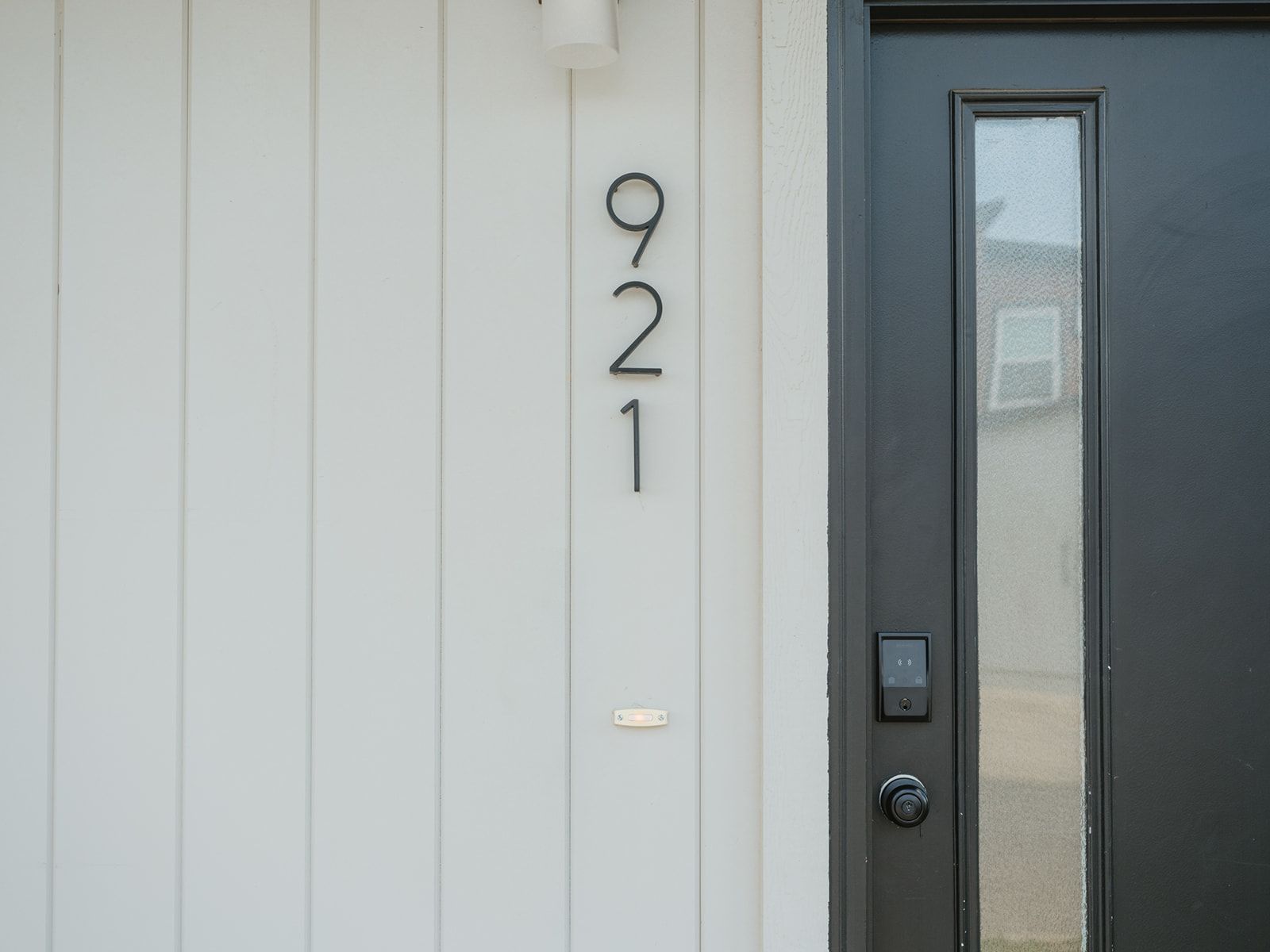 A white building with the number 921 on the wall, a dark door with a window, and a doorbell.