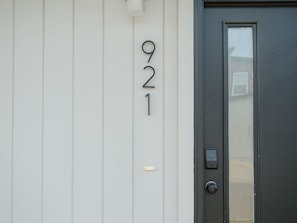 A white building with the number 921 on the wall, a dark door with a window, and a doorbell.
