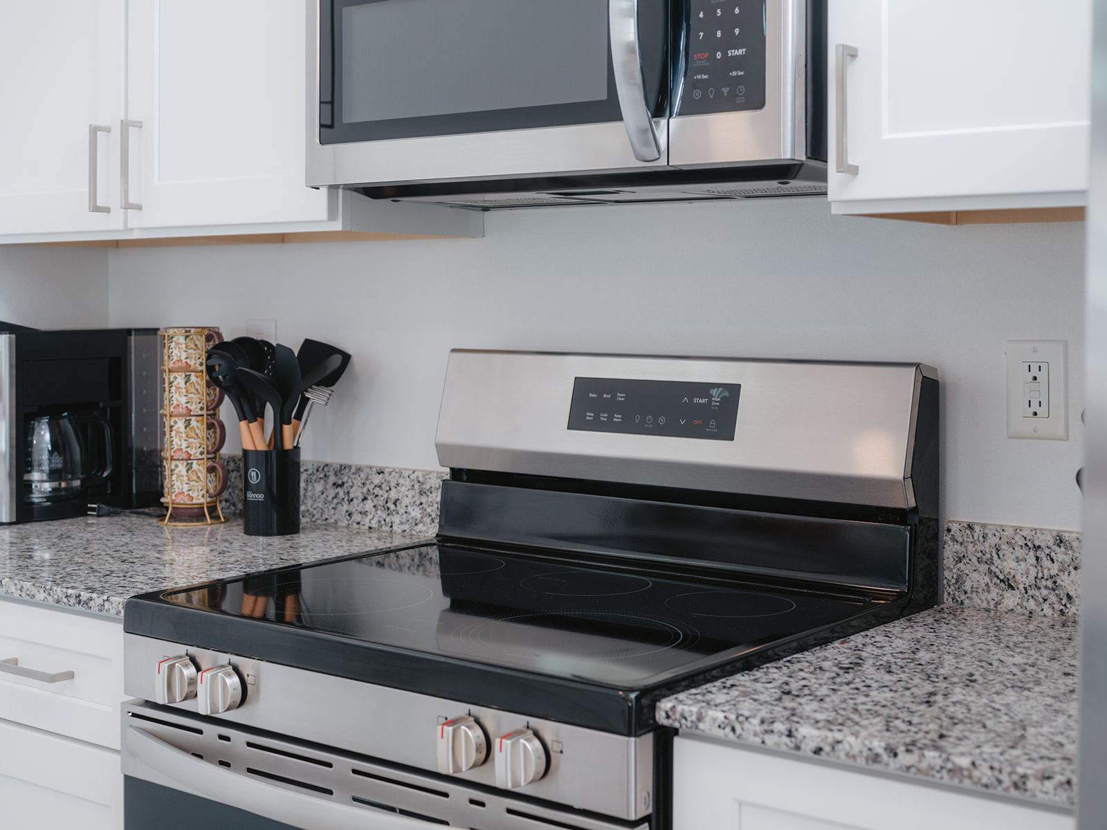 A kitchen with a stainless steel microwave, a black induction cooktop, and a granite countertop.