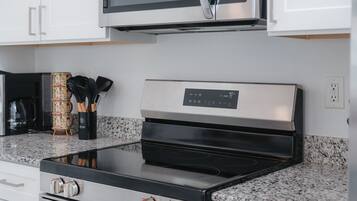 A kitchen with a stainless steel microwave, a black induction cooktop, and a granite countertop.