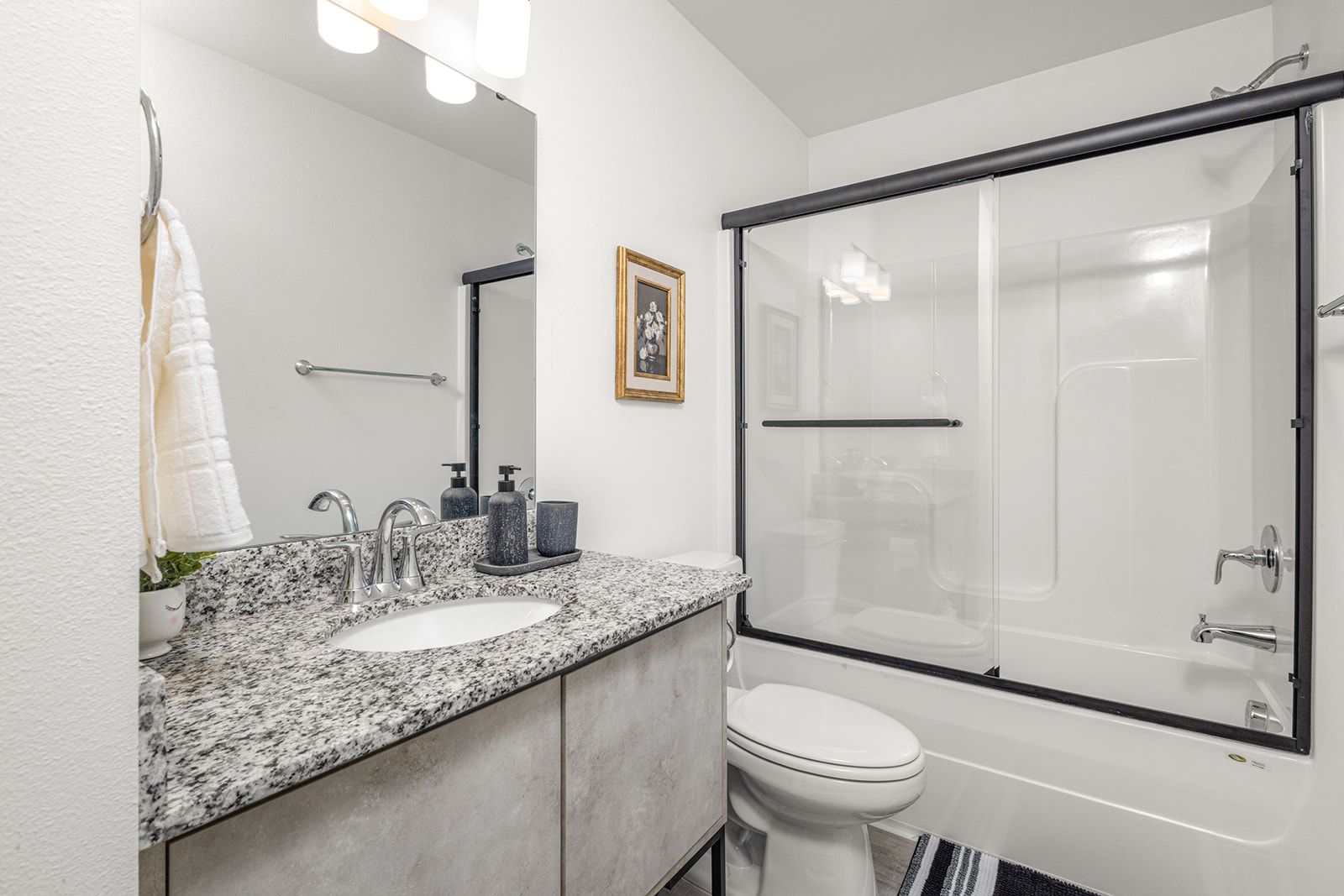 A modern bathroom with a granite countertop, a white sink, a toilet, and a glass-enclosed shower.