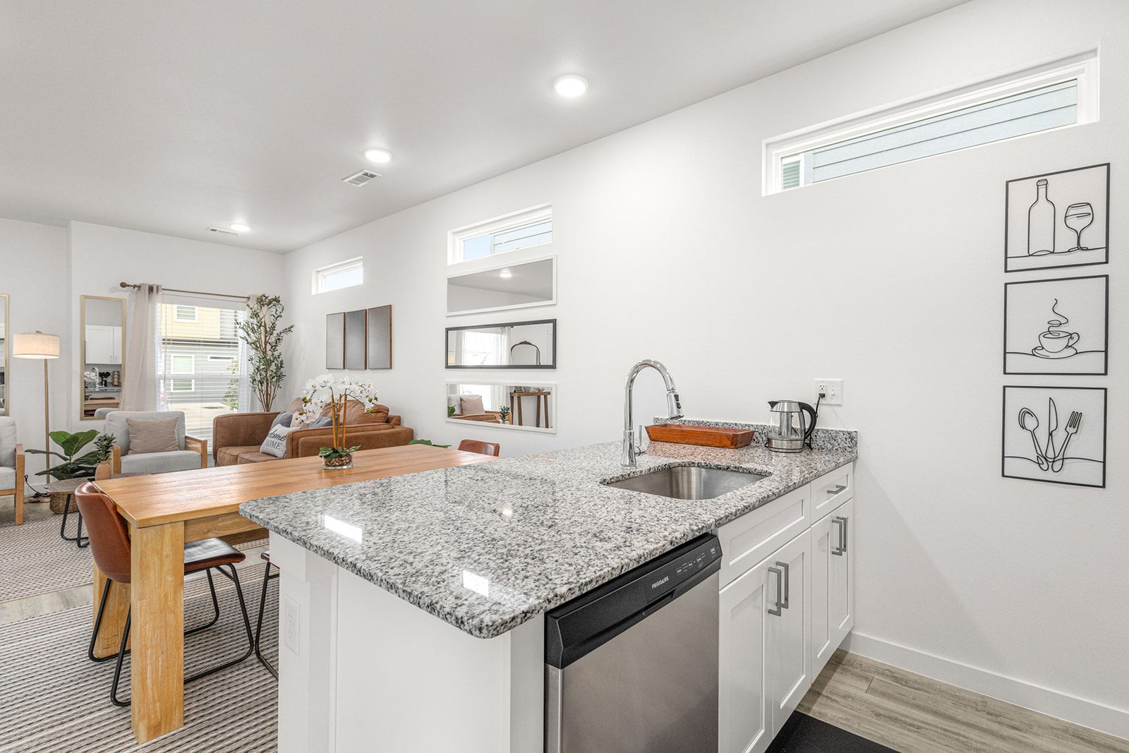 A modern kitchen with granite countertops, a dishwasher, and a dining area with a wooden table and chairs.