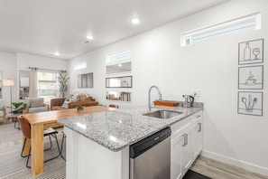 A modern kitchen with granite countertops, a dishwasher, and a dining area with a wooden table and chairs.