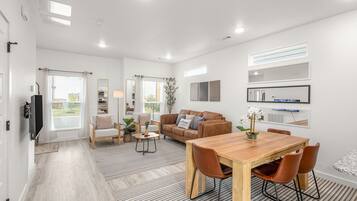 A modern living room with a sofa, chairs, a coffee table, and a dining area with a wooden table and chairs.