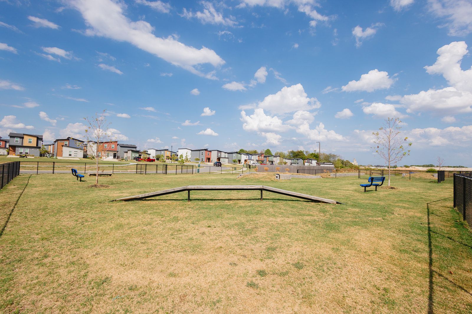 A fenced outdoor area with a grassy field, benches, and a small ramp.