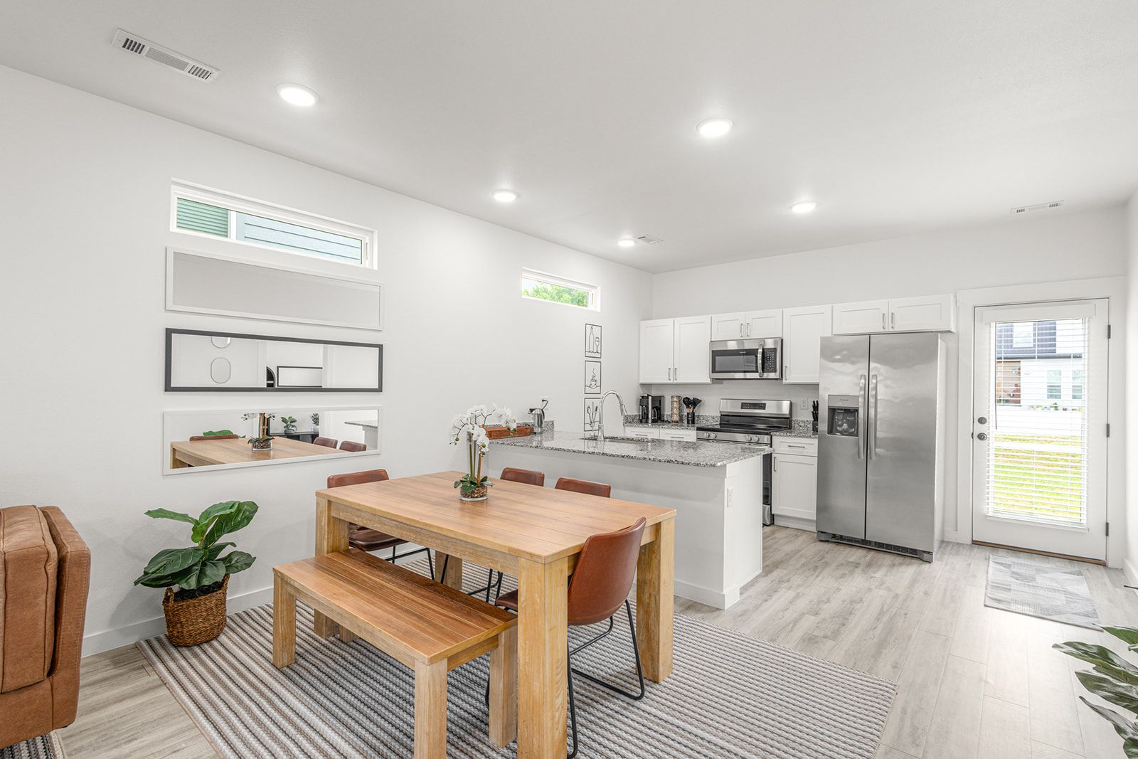A modern kitchen with white cabinetry, a stainless steel refrigerator, and a dining area with a wooden table and chairs.