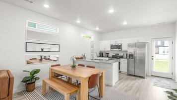 A modern kitchen with white cabinetry, a stainless steel refrigerator, and a dining area with a wooden table and chairs.