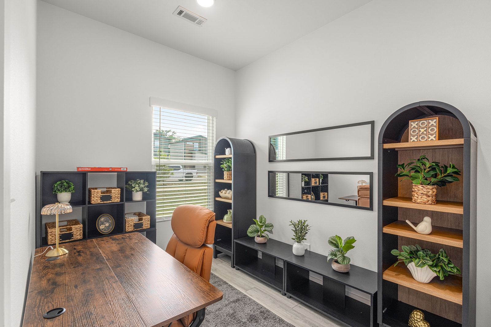 A modern office space with a wooden table, a leather chair, and built-in shelving with potted plants.