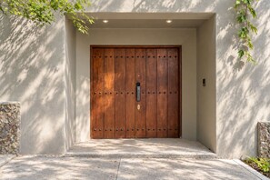 Una puerta de madera con un ojo de cerradura y cerradura, ubicada en un acceso de concreto con detalles de piedra.