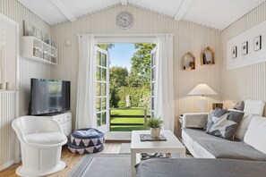 Een gezellige woonkamer met een televisie, zithoek en uitzicht op een tuin.