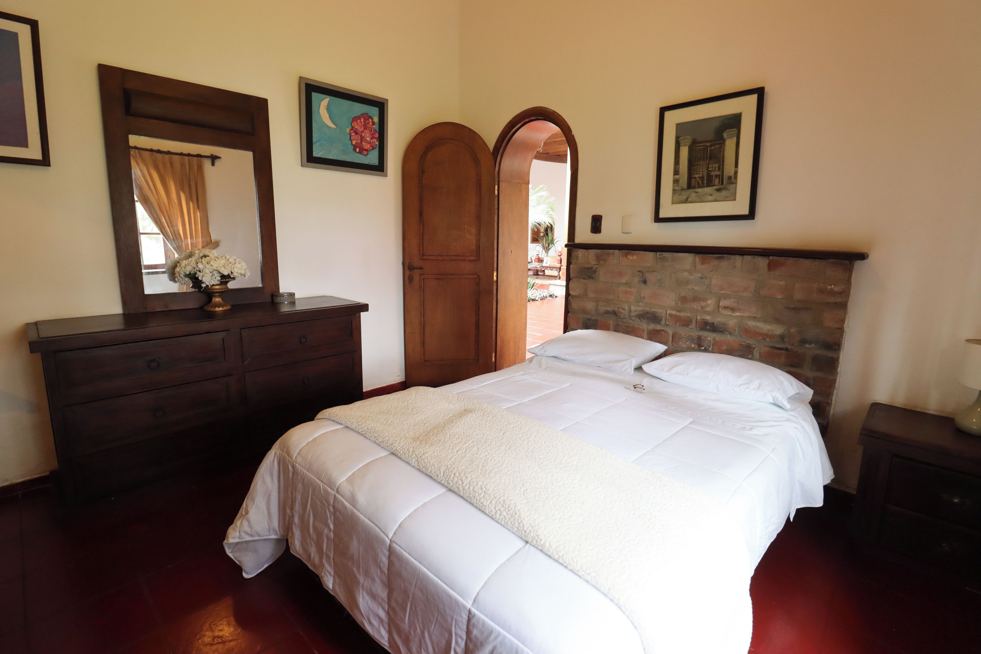 Een slaapkamer met een bed, een dressoir, een spiegel en een bakstenen muur.