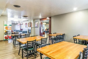 Un restaurante con mesas y sillas de madera, pared de ladrillo y un tablero con la carta.