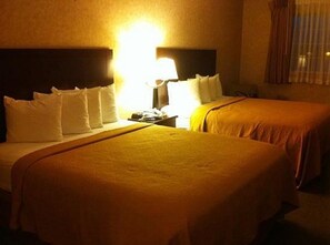 Quarto de hotel com duas camas, uma mesa de cabeceira e uma luminária.